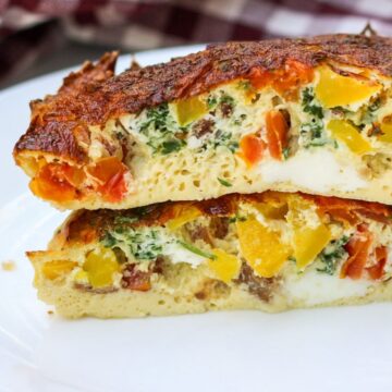 Two large omeltte halves are stacked on each other facing the cut side towards the camera lense. The omelette is fluffy and thick with visible yellow, red and green vegetables inside and golden brown top.