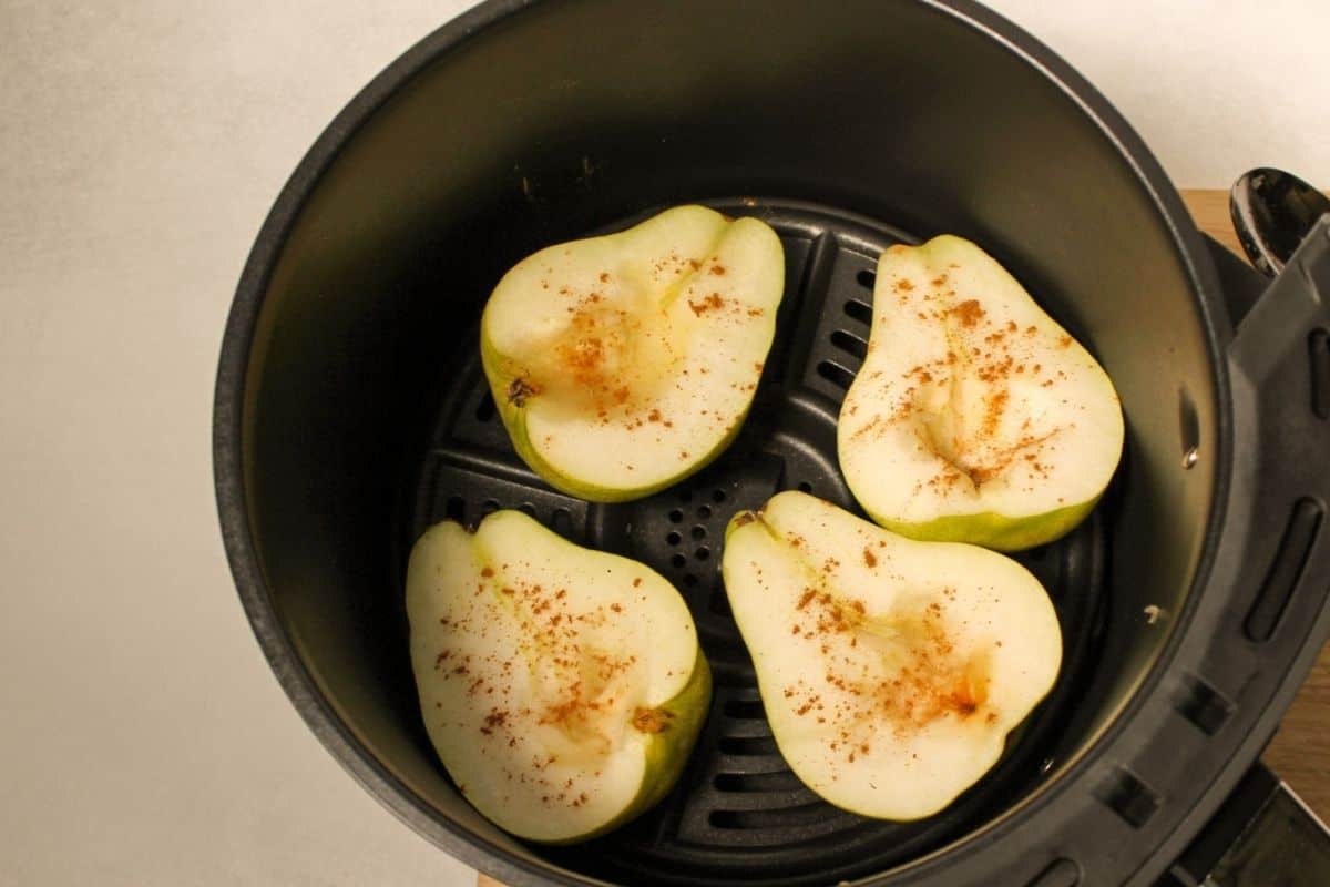 Process shot #3: pear halves arranged in air fryer basket, facing the cut side up. There is some spices on top of the pears.