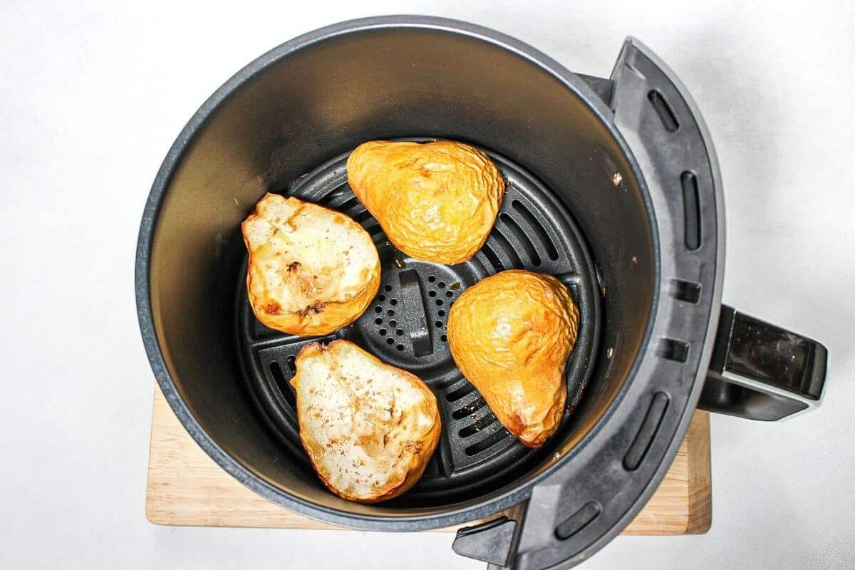 Process shot #5: visibly cooked yellow pear halves in air fryer black basket. Two are facing the cut side up and the other two facing the cut side down.