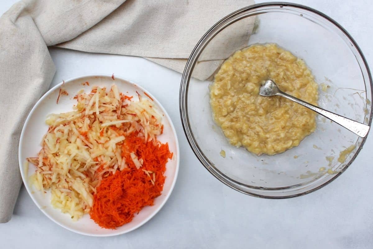 Process shot 2: a glass bowl with a mashed banana and a fork. A white flat plate with shredded carrots and apples.