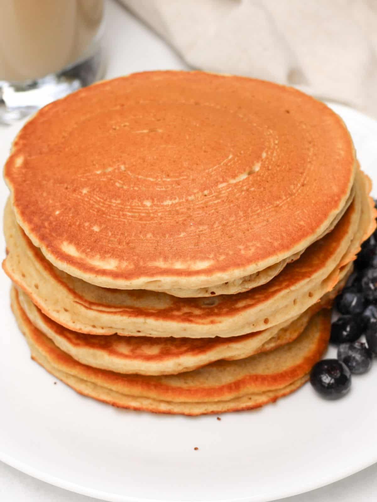 A stack of plain pancakes on a white plate with some fresh blueberries on a side.