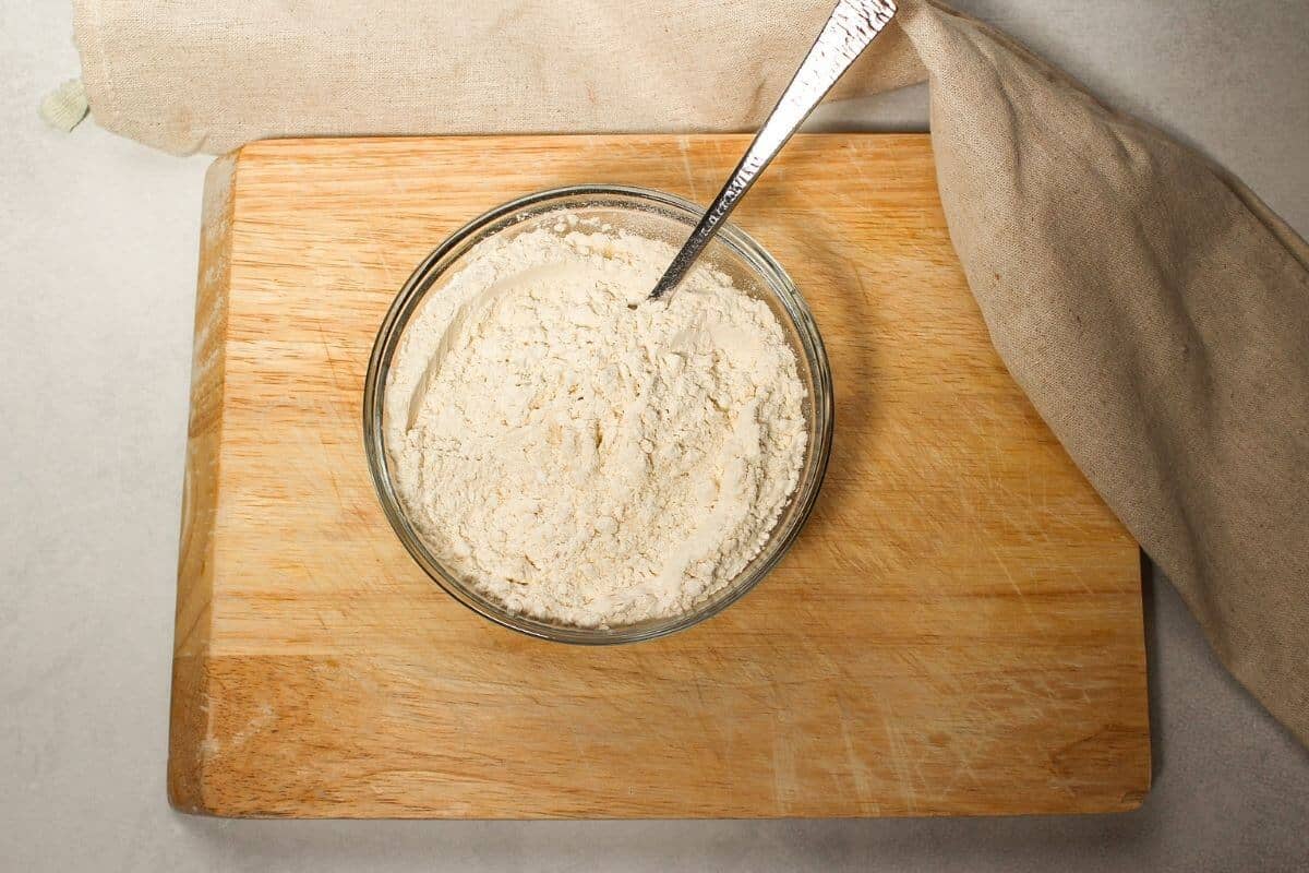 Process image with a glass bowl full of white flour on a wooden cutting board.