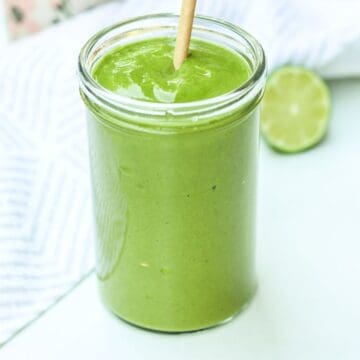 A bright green smoothie in a tall glass with the straw. There is half of the lime behind it.