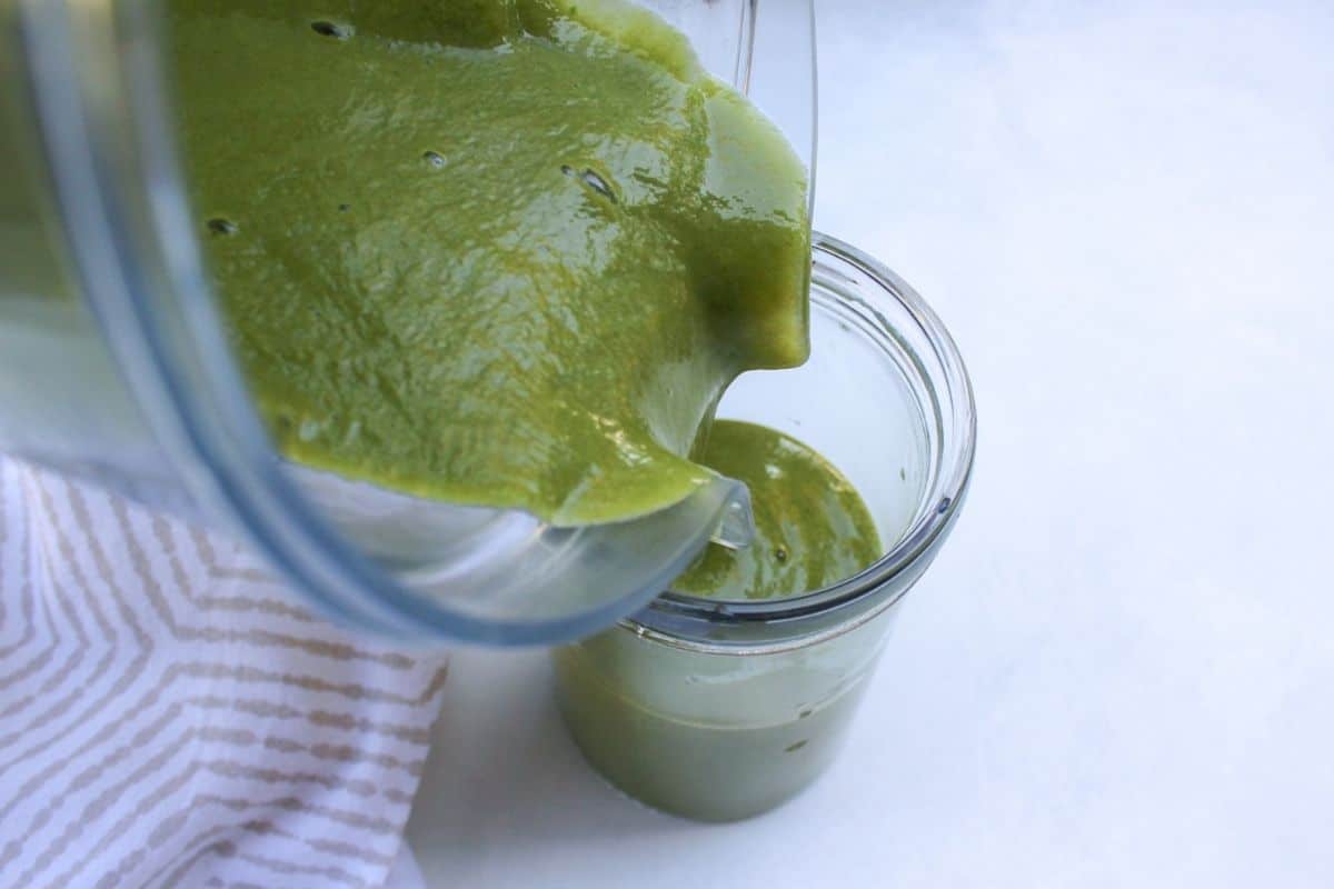 Process shot #3: close up shot of a green smoothie being poured into the glass from a blender container.