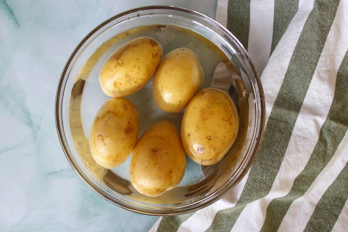 A glass bowl with five potatoes sumberged in water.