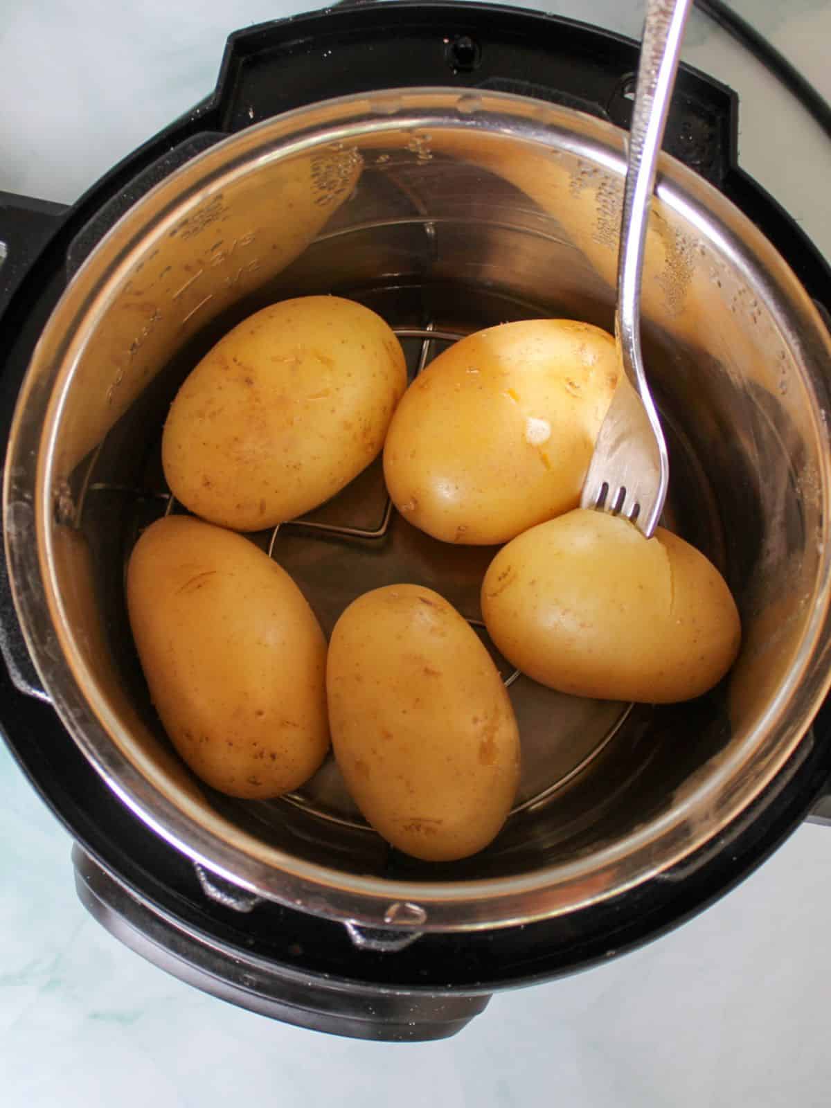 Overhead shot of five whole potatoes inside the instant pot. There is a fork pierced in one of the potatoes to show doneness.