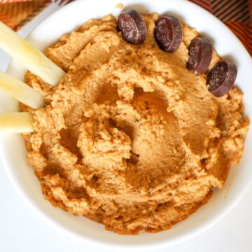 A white bowl with thick orange dip. There are 4 chocolate coins on the top side dipped into the dip.