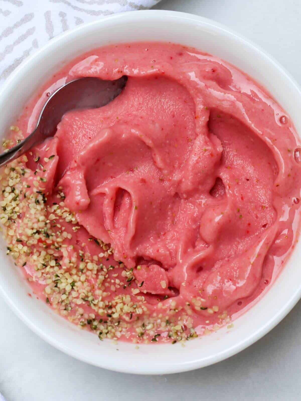 A white bowl with some pink thick watermelon smoothie topped with some hemp seeds on the left side.