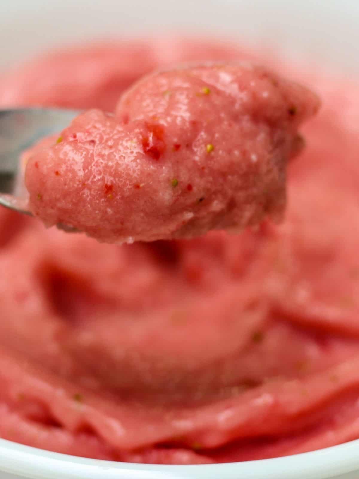 A close up shot of a spoon with some pink smoothie.