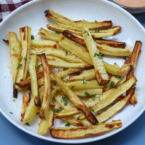 Crispy parsnips sprinkled with chopped green parsley, served on a white plate.