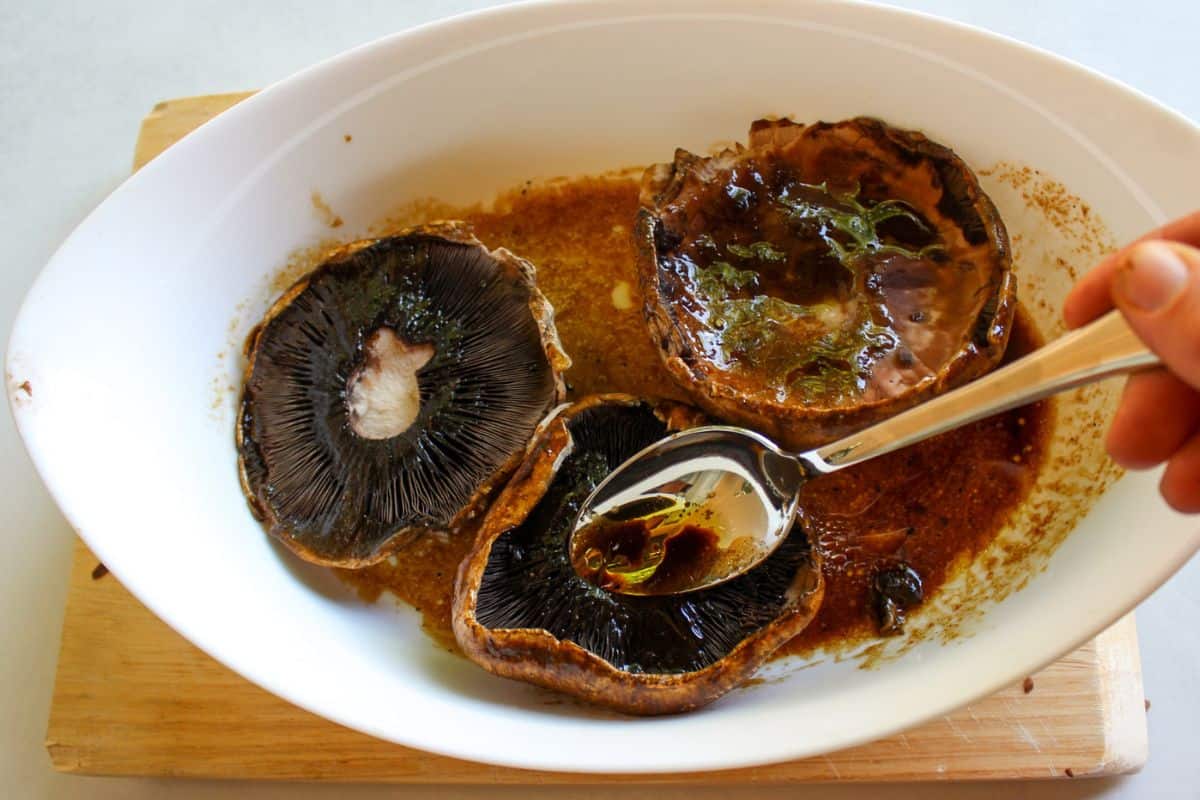 Three mushrooms in a shallow dish with marinade.