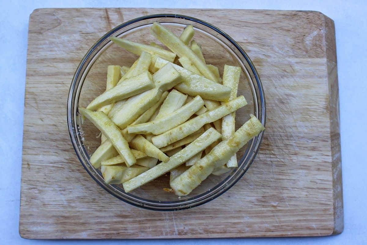 Cut parsnips in a large glass mixing bowl on a wooden cutting board.