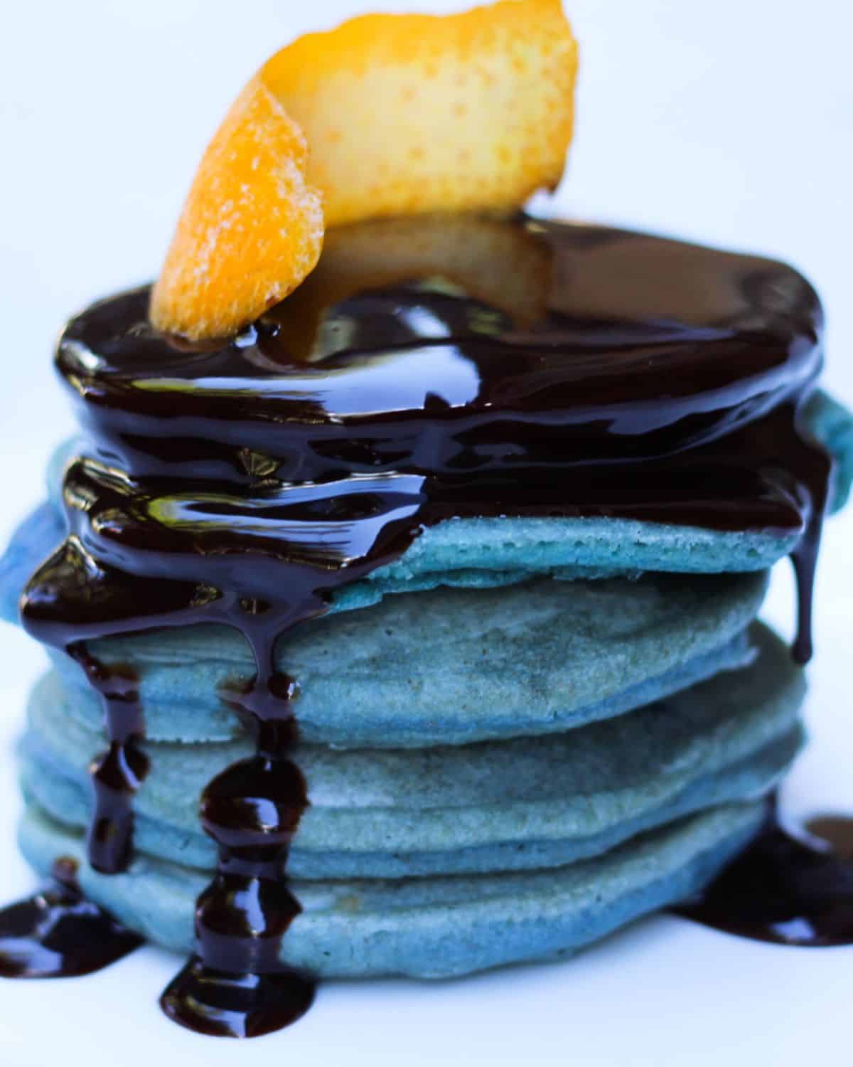 Stacked pancakes covered with chocolate and have an orange rind on top.