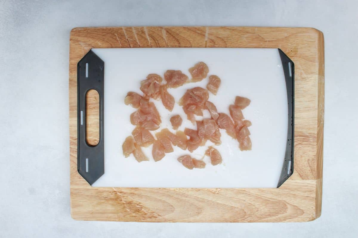 A white cutting board with finely diced raw chicken.