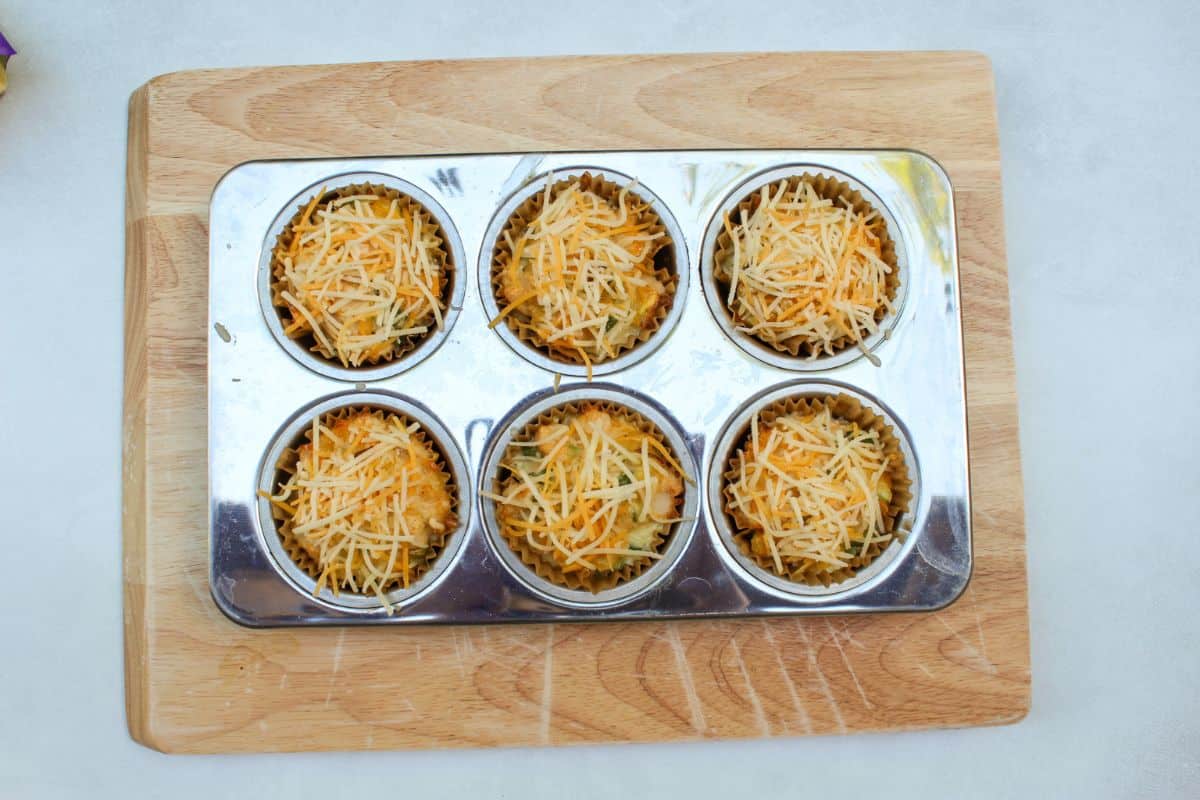 A pan with cooked chicken muffins topped with fresh shredded cheese.