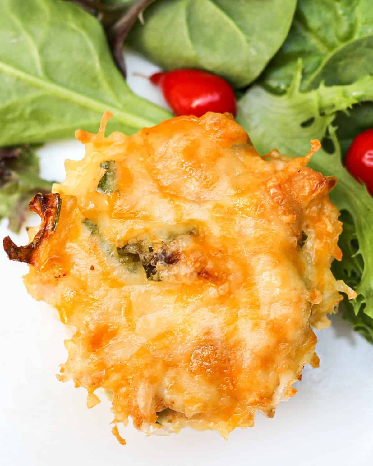 The top view of one savory muffin with cheese on top. There is a green salad on the side.