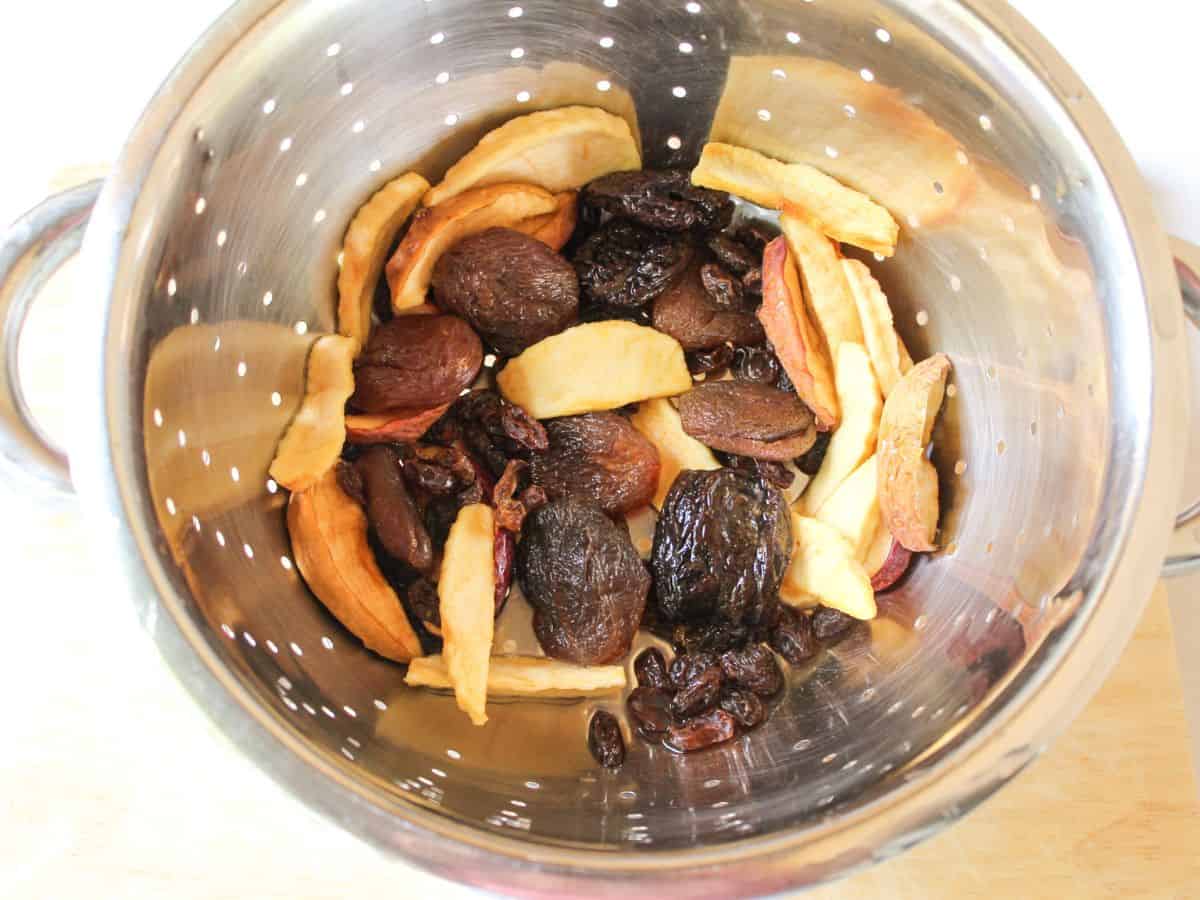 A stainless steel colander with different dried yellow and dark brown fruits.