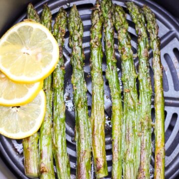 Roasted asparagus spears on the air fryer basket with fresh sliced lemon on a side.