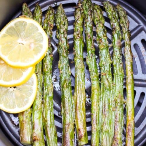 Roasted asparagus spears on the air fryer basket with fresh sliced lemon on a side.