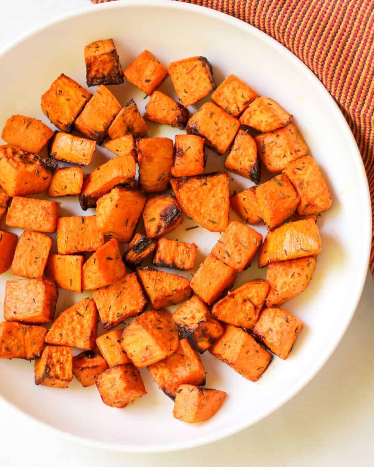 Orange roasted vegetable cubes on a white plate.