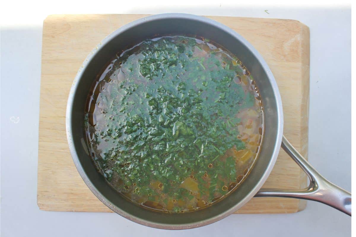 Overhead view of a large pot filled with liquid and a lot of fresh chopped greens on top.