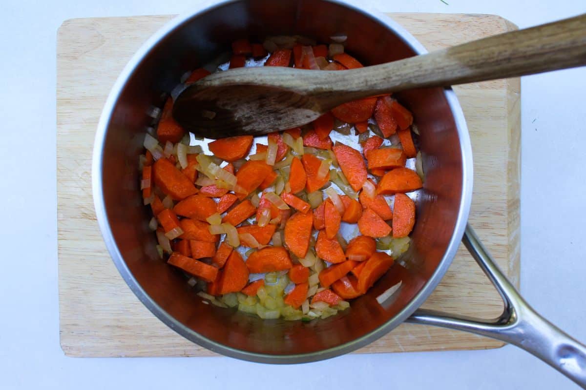 Overhead view of a large pot with sauteing carrots and onions. There is a wooden spoon in a pot.