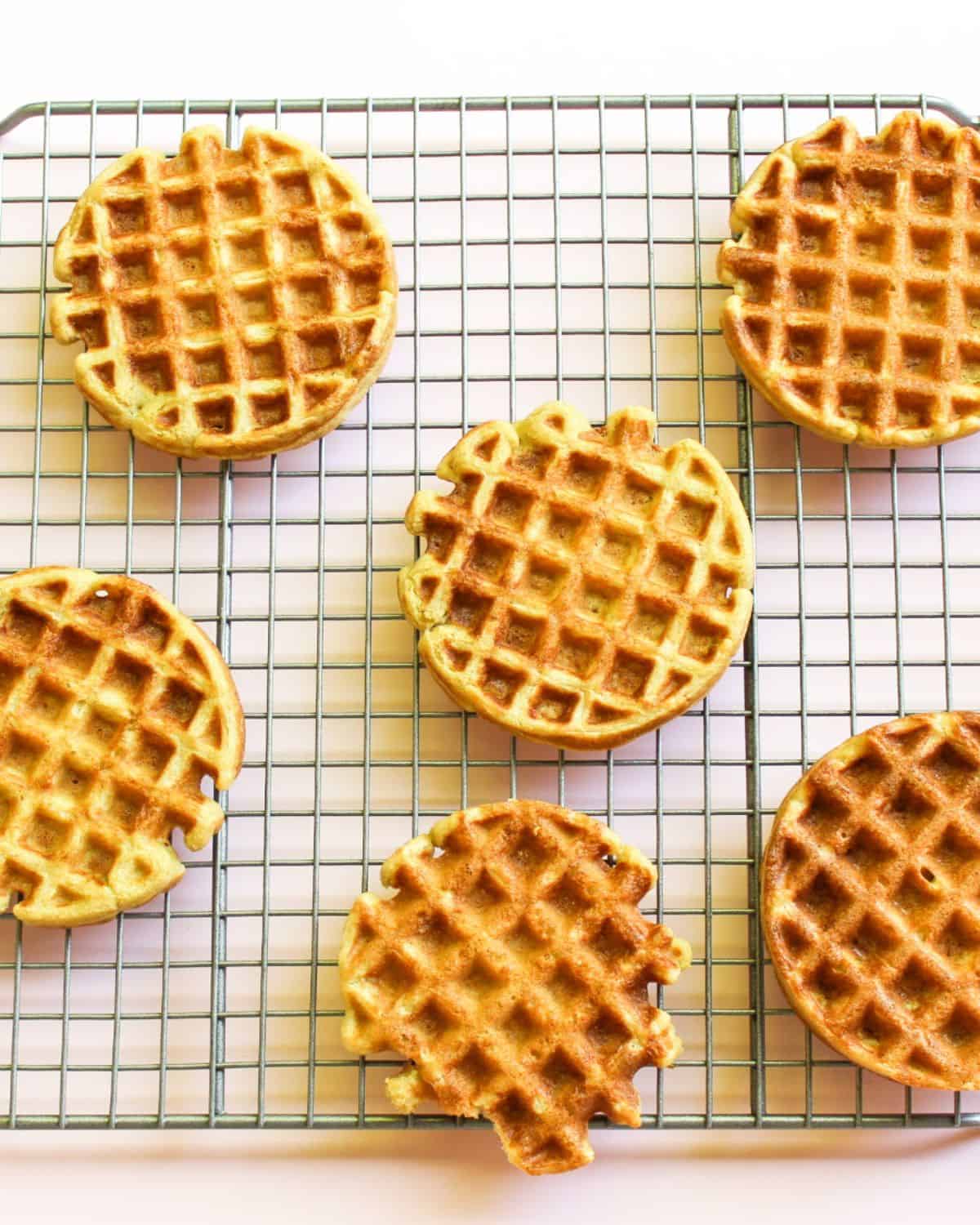 Six golden waffles are arranged on a wire rack.