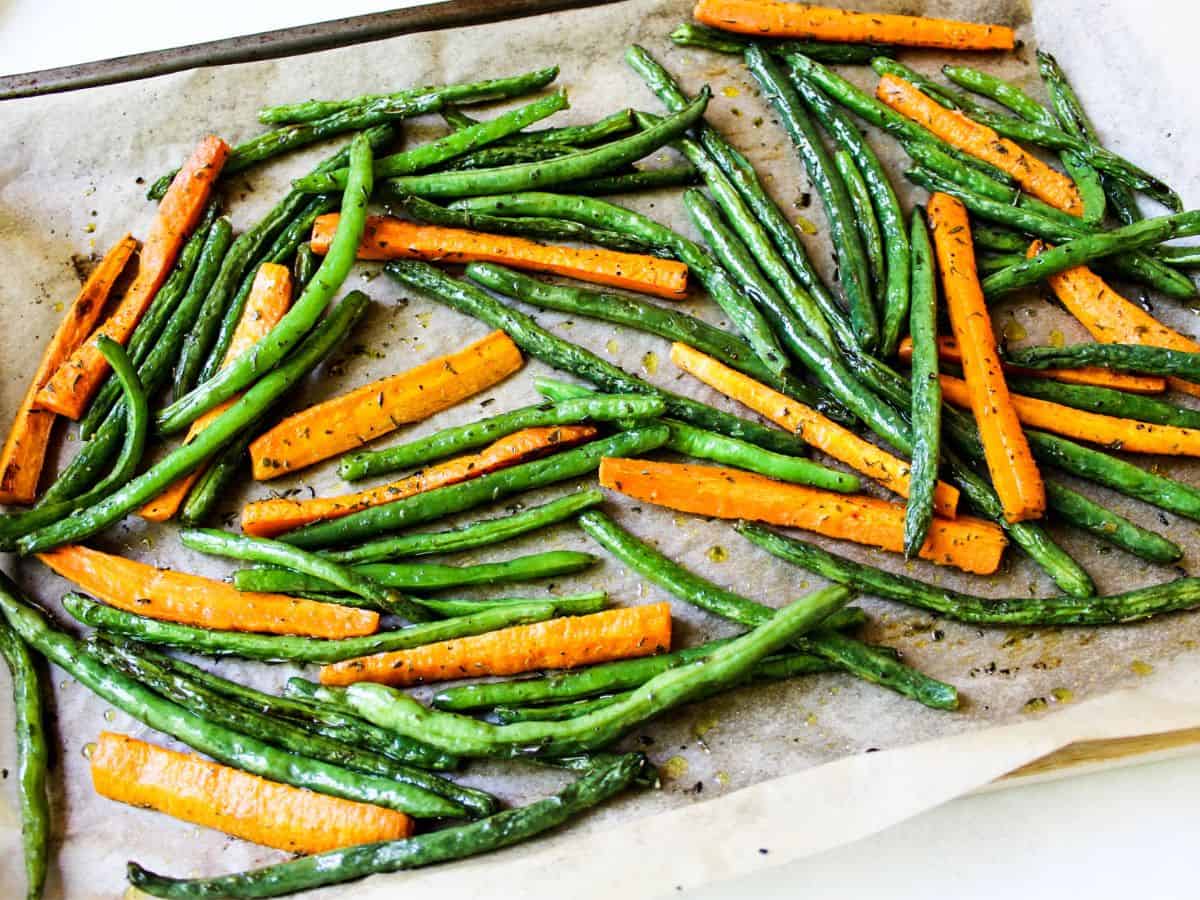 Roasted green and orange veggies on a large baking pan laid with parchment paper.