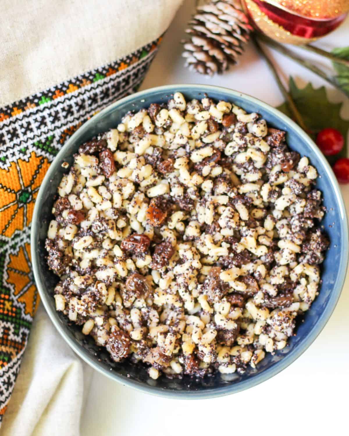 Overhead view of a blue bowl with a yellow, brown, and black grain dish. There is Ukrainian embroidery on the left side and some Christmas pine cone on top.