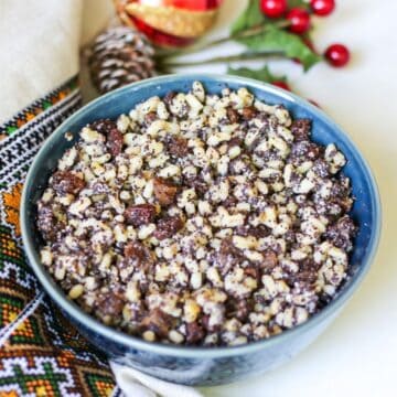 A blue bowl filled with cooked grains, fuits and seeds. There is Ukrainian embroidery towel on the left side and red Christmas ornaments on the top.