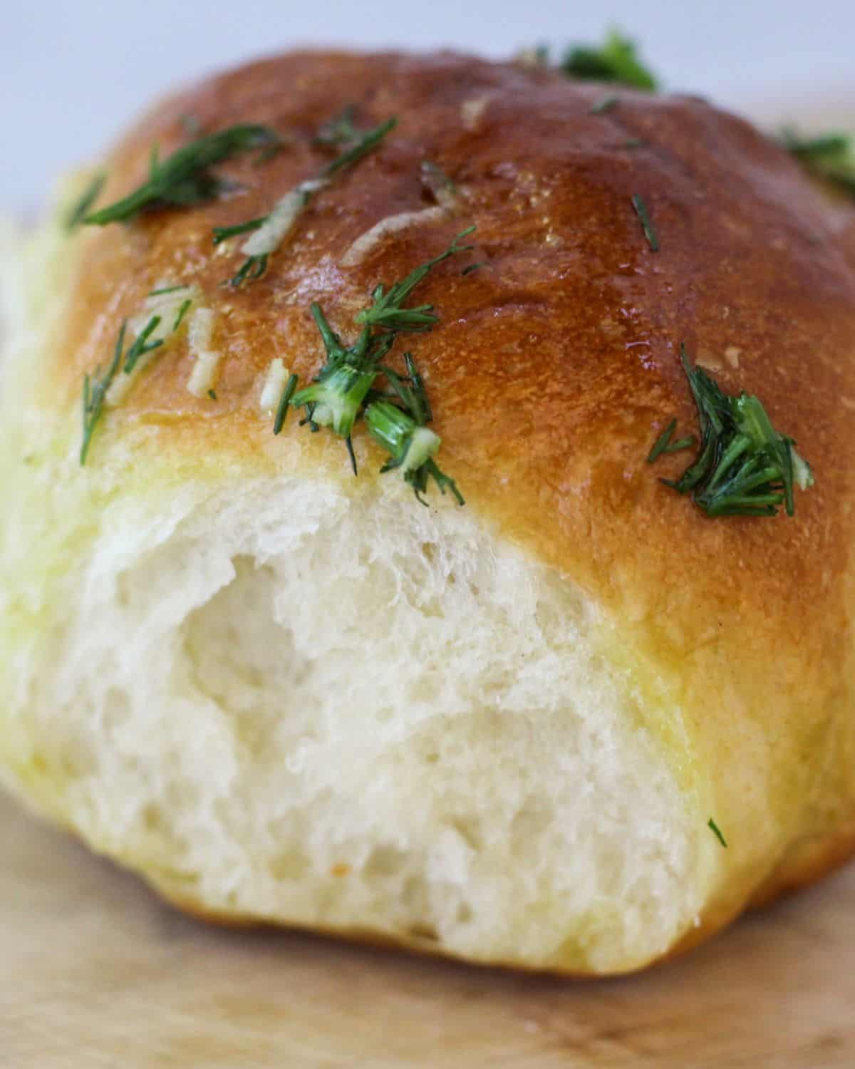 A single bread roll with a golden top crust on a wooden surface.