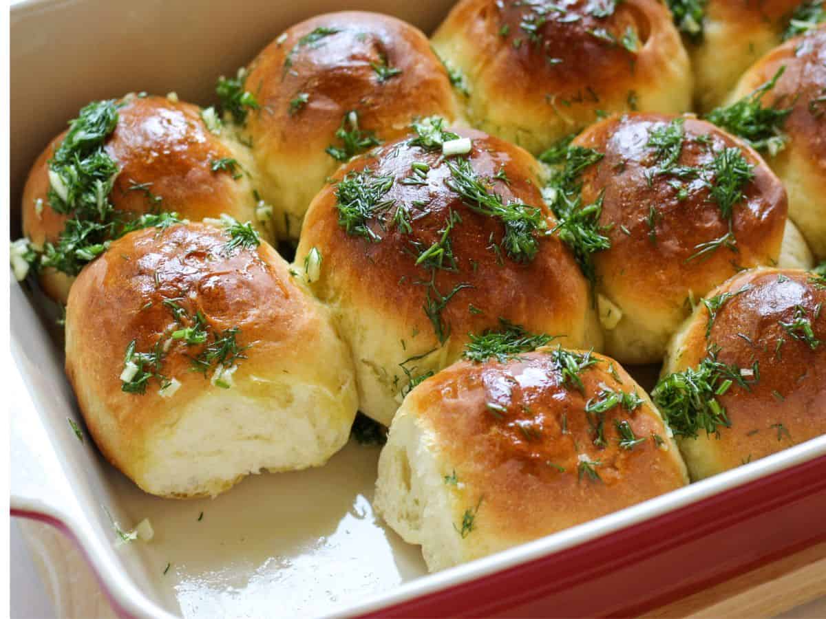 Golden brown bread rolls in a baking dish topped with chopped dill.