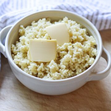 Cooked millet grain in a bowl with two side handles. There are two slices of butter on top.