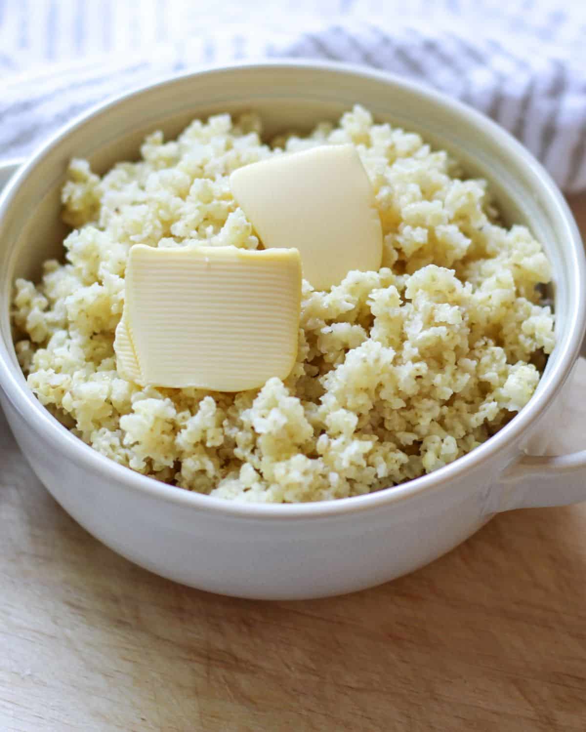 Cooked millet grain in a bowl with two side handles. There are two slices of butter on top.