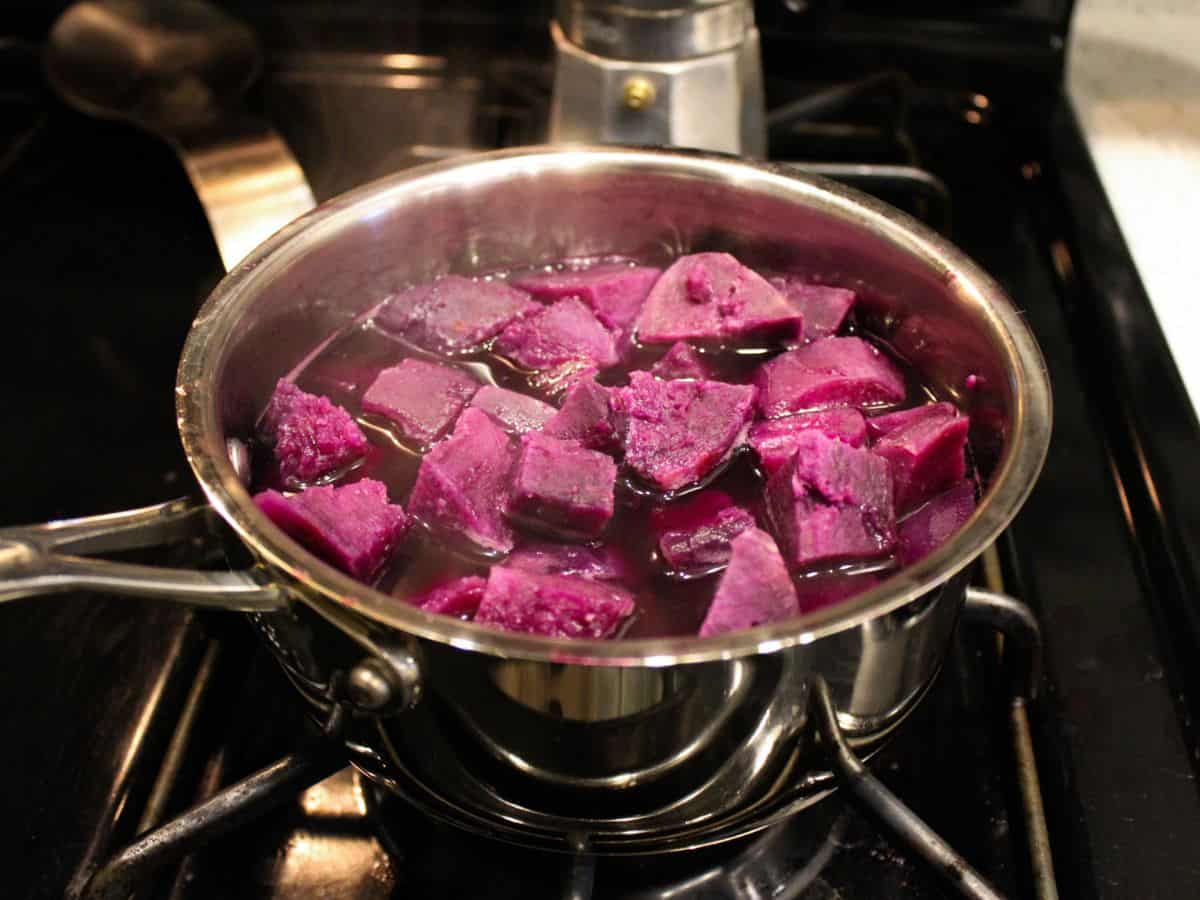 A stainless steel pot on the stove filled with water and chunks of purple vegetables. The steam is coming from the pot.
