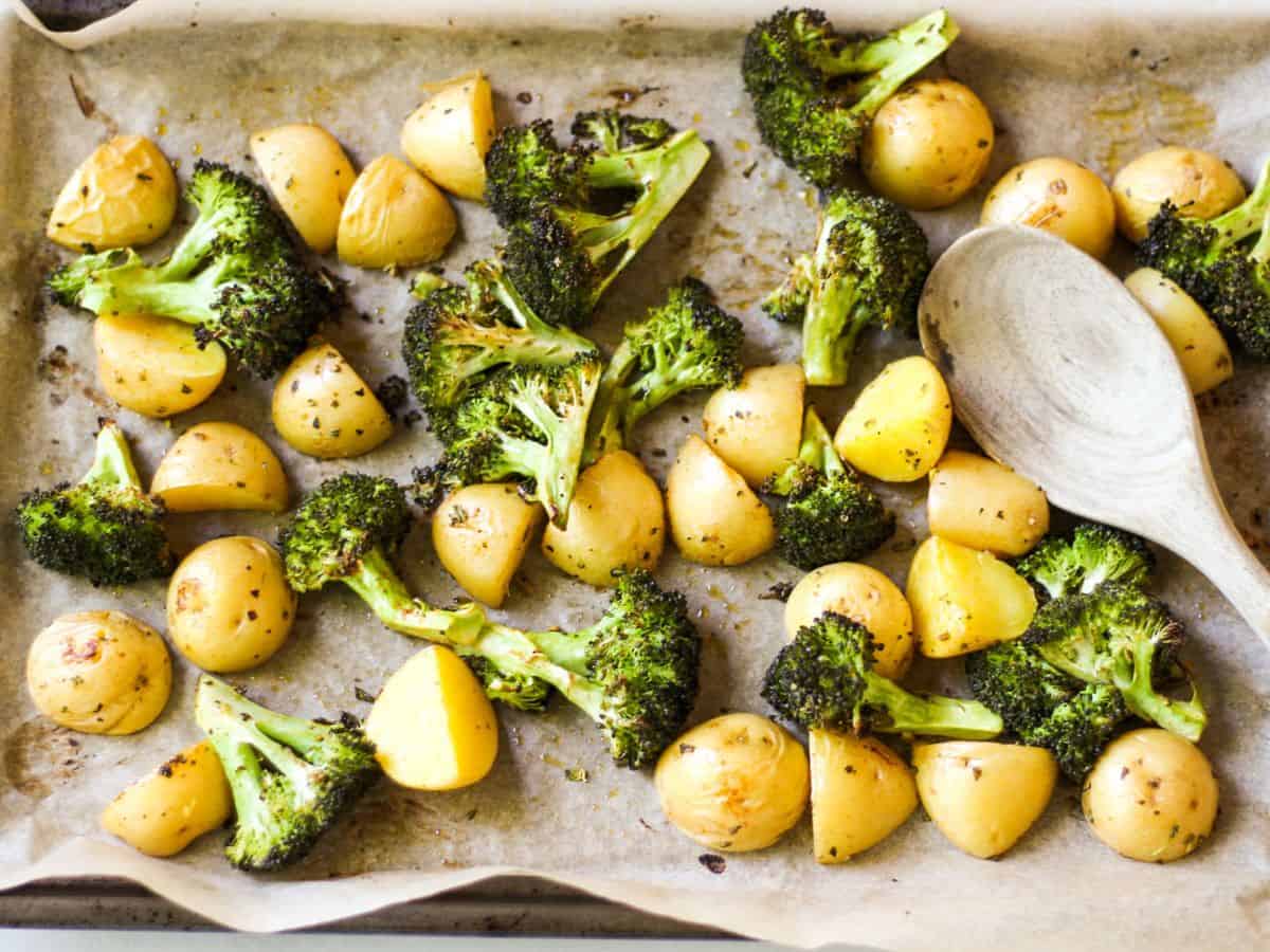 A sheet of parchment paper with cooked crispy broccoli florets and yellow potatoes.