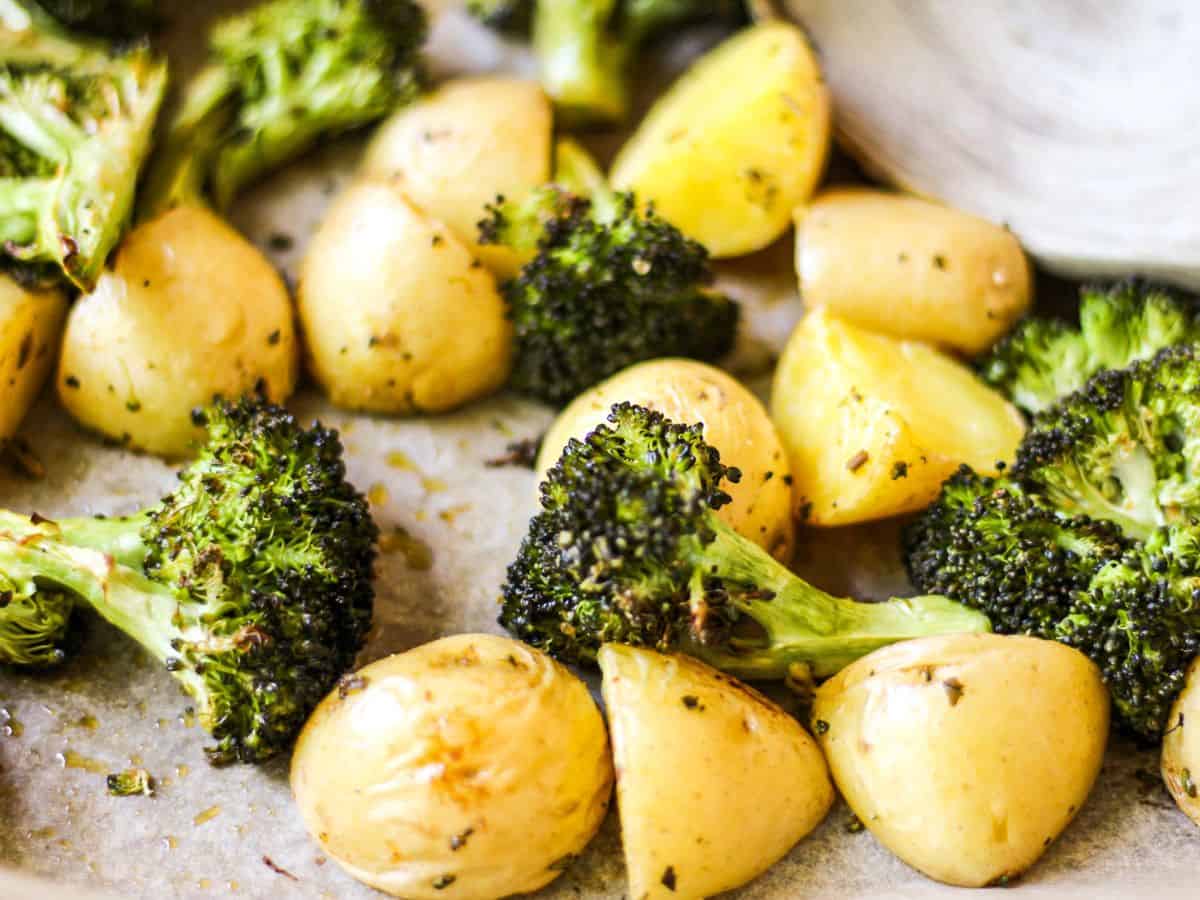 Roasted broccoli florets and yellow halved potatoes on parchment paper.