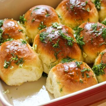 Golden brown bread rolls in a baking dish topped with chopped dill.