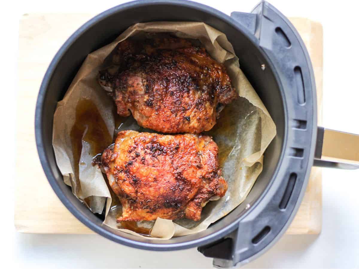 Air fryer basket covered with parchment paper with two roasted seasoned thighs.