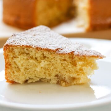 A slice of fluffy yellow cake dusted with powdered sugar on a white plate.