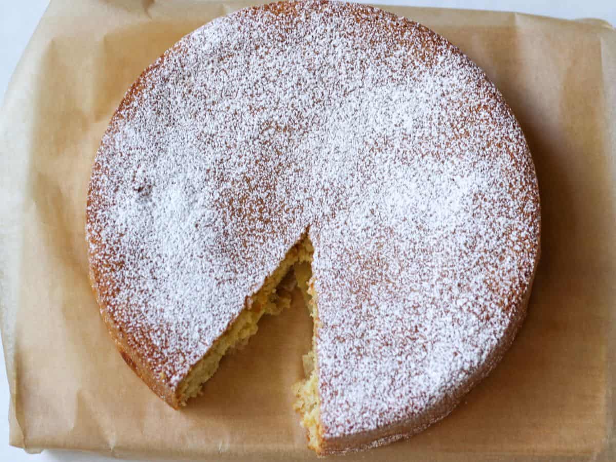 A round cooked baked cake dusted with powdered sugar on top. It is placed on parchment paper.