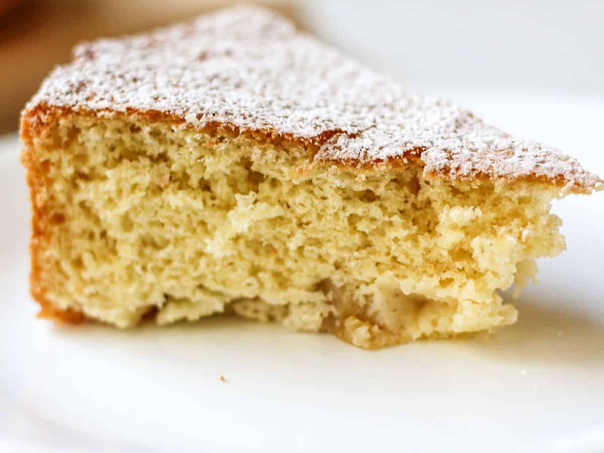 A slice of fluffy yellow cake dusted with powdered sugar on a white plate. 