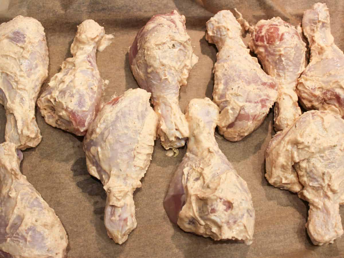 Uncooked chicken legs in yogurt marinade arranged on a parchment paper.