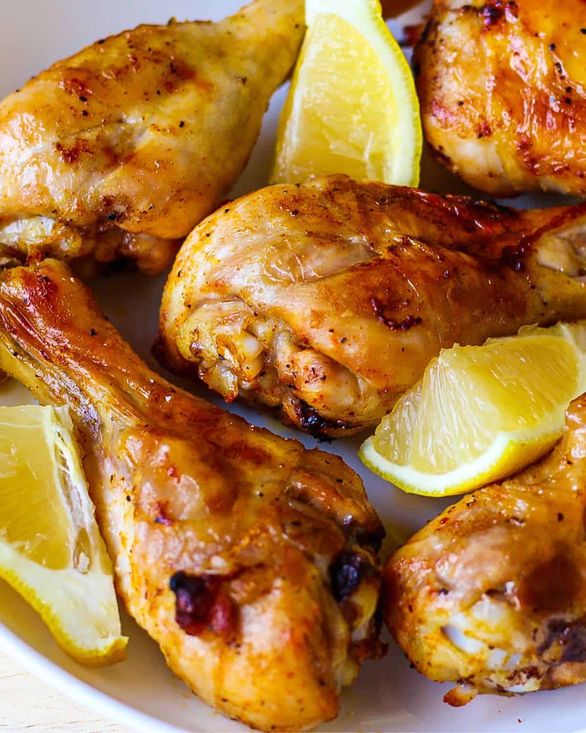 Close-up view of cooked chicken legs with a few fresh lemon wedges and specks of black pepper on top.