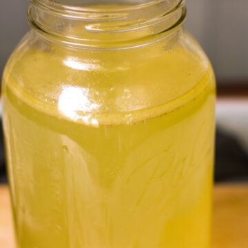 A glass clear large jar filled with yellow stock.