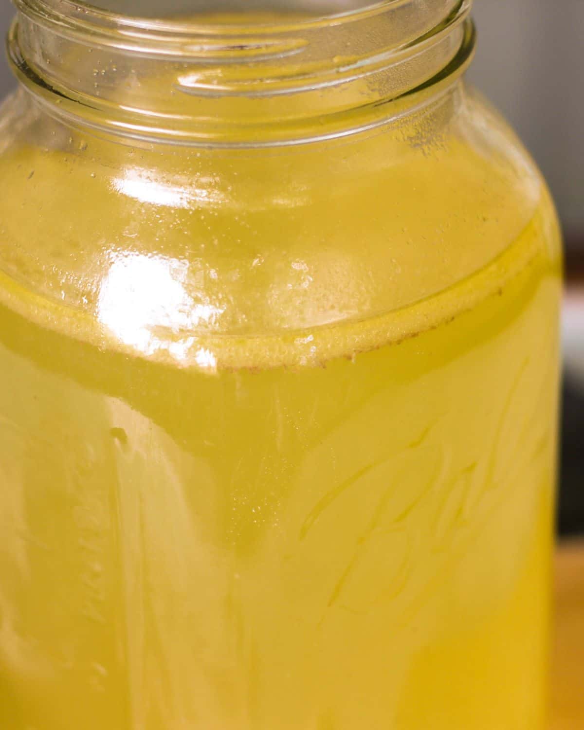 A glass clear large jar filled with yellow stock.