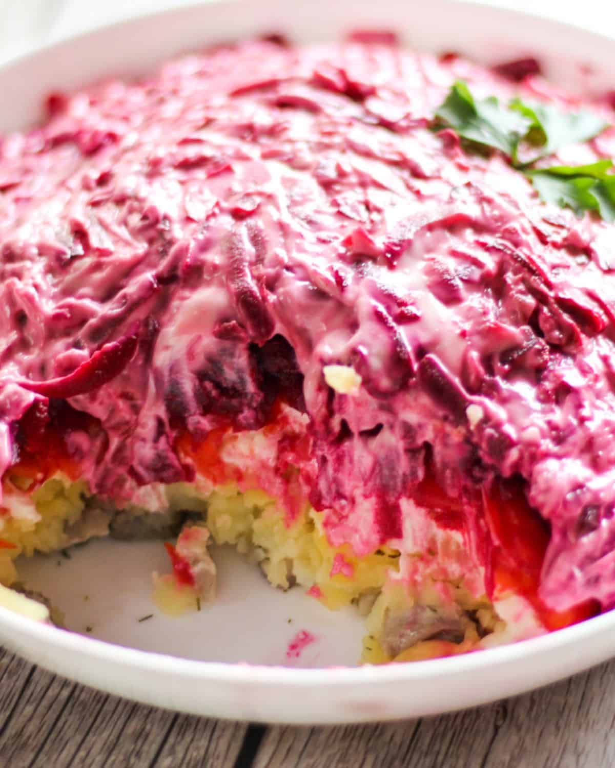 A layered salad with herring, potatoes, carrots and beets covered with mayo.