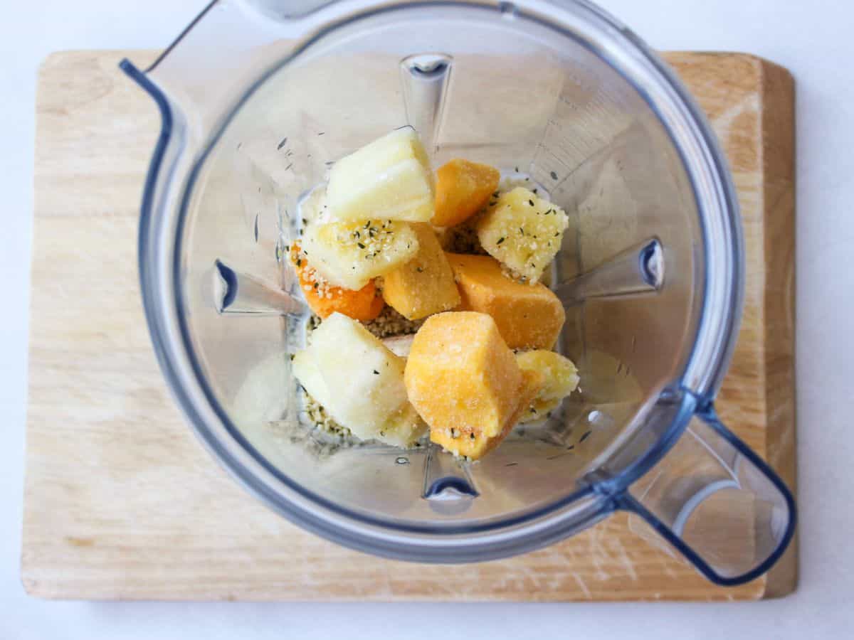 Blender container with chunks of yellow and orange fruits and some seeds.