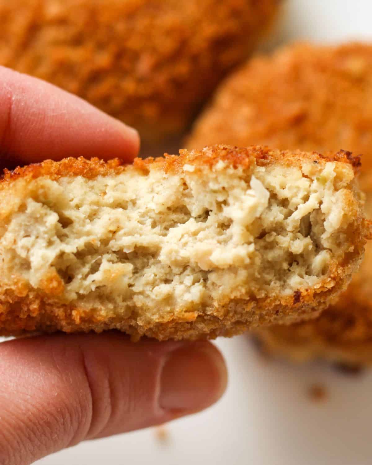 A hand holding a meat patty with few bites taken showing the inside of the rissole.