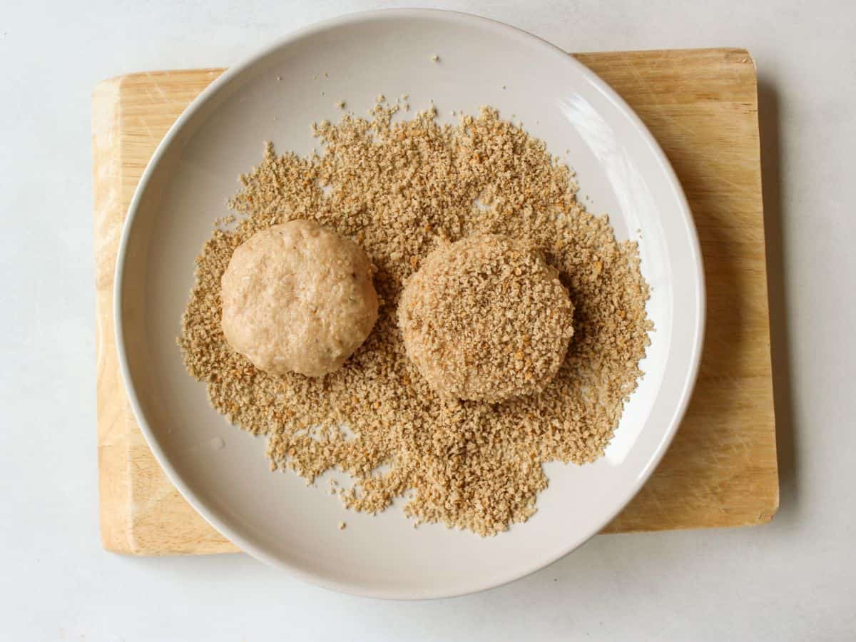 A shallow dish with bread crumbs and two coated rissoles.